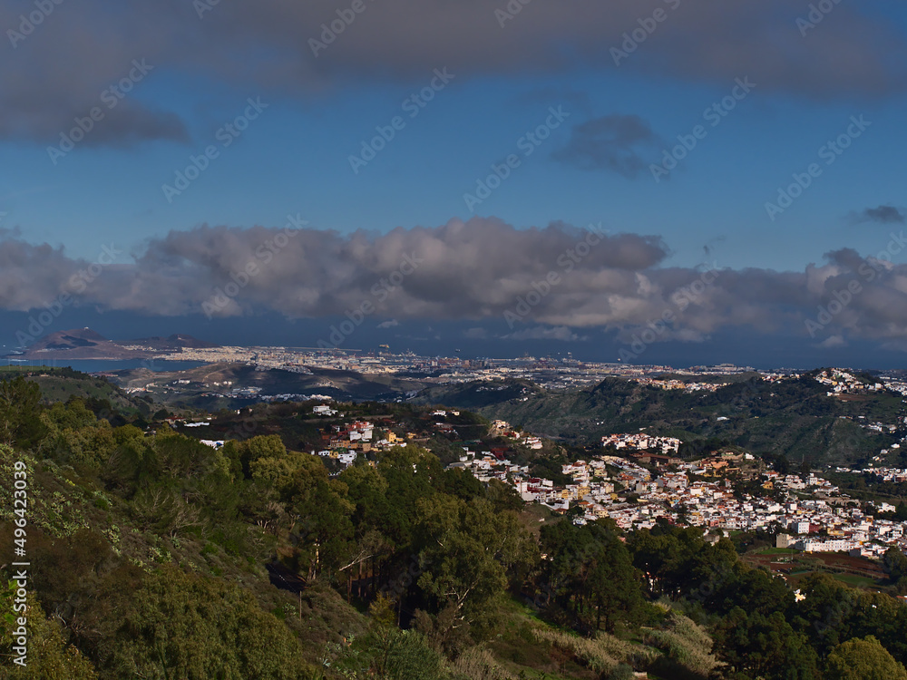 View over the northeast of island Gran Canaria, Spain with small village Teror surrounded by green hills and capital city Las Palmas in background.