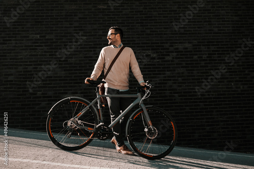A fashionable man pushing bicycle on the street.