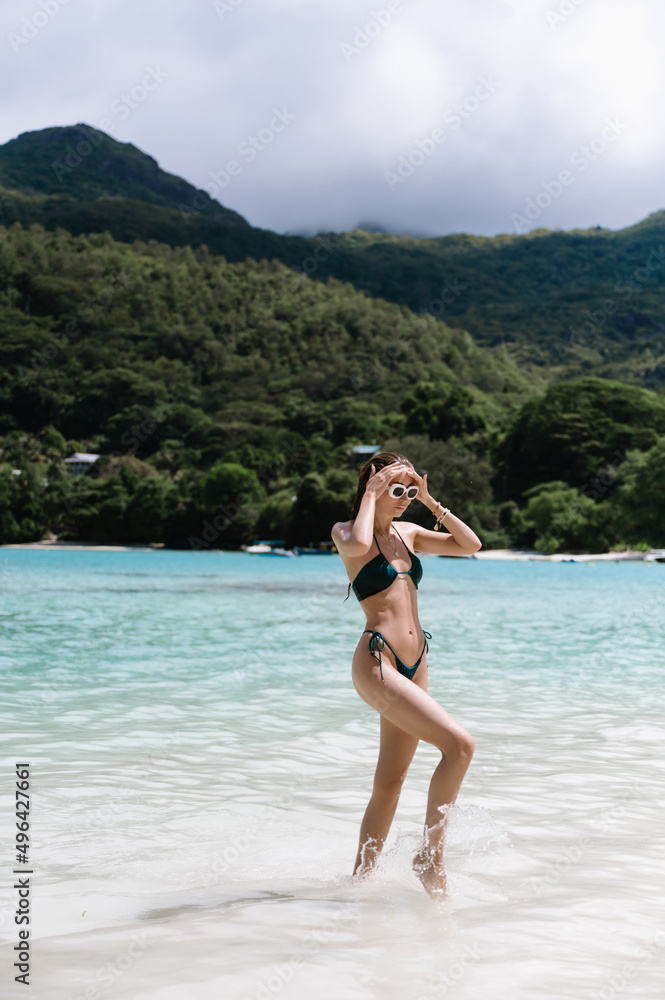 Beautiful young woman in green emerald bikini swimsuit on Seychelles beach on Mahe or La Digue island