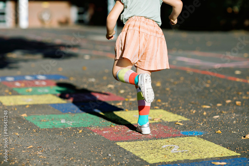 Closeup of leggs of little toddler girl playing hopscotch game drawn with colorful chalks on asphalt. Little active child jumping on playground outdoors on a sunny day. Summer activities for children.