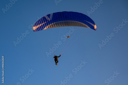 Silhouette of a man on a paraglider flying in the blue sky.