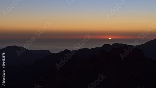 Panoramic view over the rugged mountains of island Gran Canaria, Canary Islands, Spain at sunset with colorful sky and sun going down on the horizon.