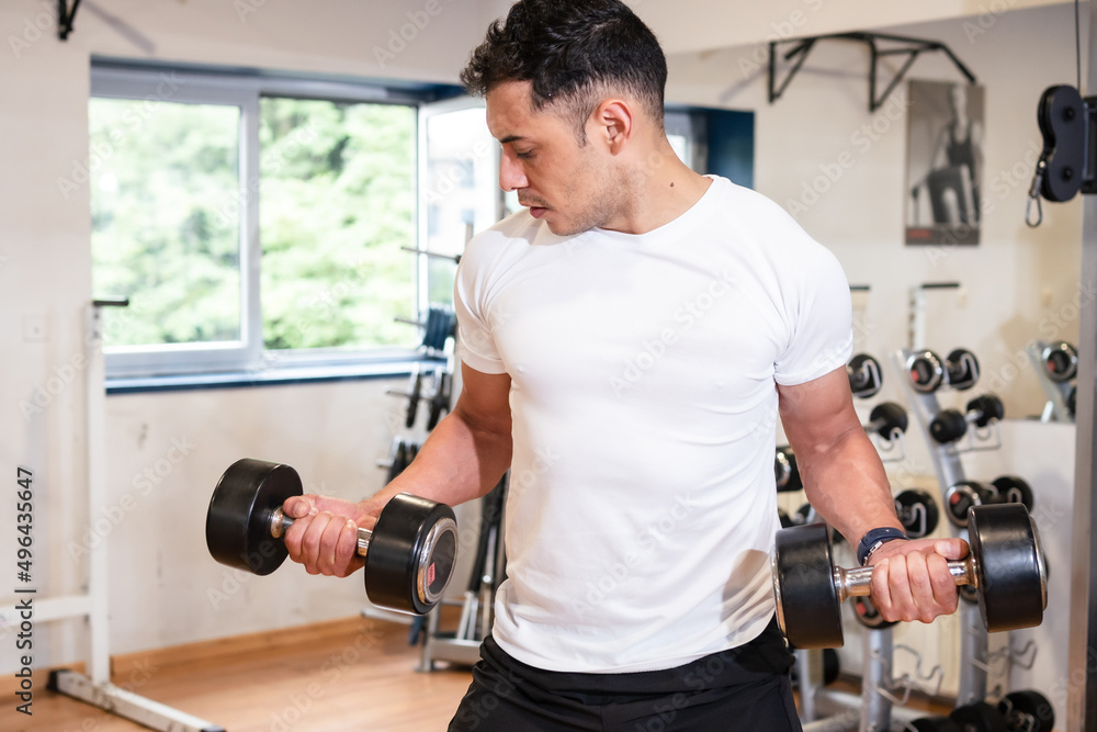 A caucasian man in the gym in a white t-shirt lifting weights, healthy and healthy life doing sports A caucasian man in the gym in a white t-shirt lifting weights, healthy and healthy life doing sports