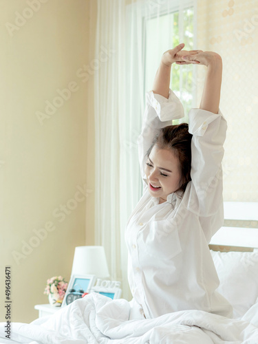 Beautiful Asian women smiling face stretching after wake up enjoying sunny morning on the bed