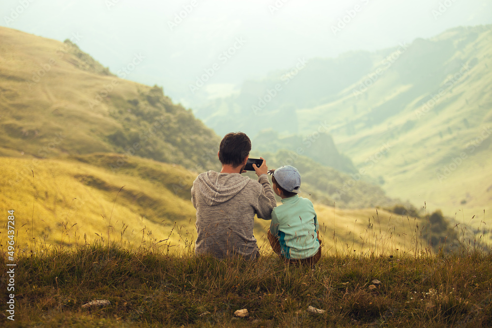 Men and boy sitting on the edge of the hill, taking photo and looking. Father and son
