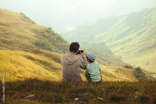 Men and boy sitting on the edge of the hill, taking photo and looking. Father and son photo