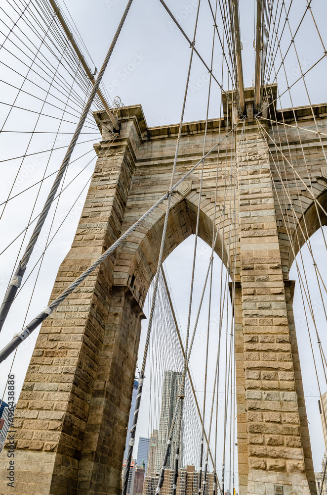 Fototapeta premium Brooklyn Bridge New York City Tower with steel wire in the forefront, view from low angle, overcast during winter day, vertical