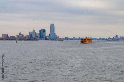 Yellow Staten Island Ferry on Hudson river in front of Jersey City in the evening, New York, during winter with overcast, wide angle shot, horizontal