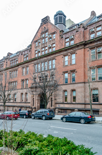 The Gottesman Libraries Building Facade with cars parked in forefront, New York City, during winter day with overcast, Plants and trees in front, vertical