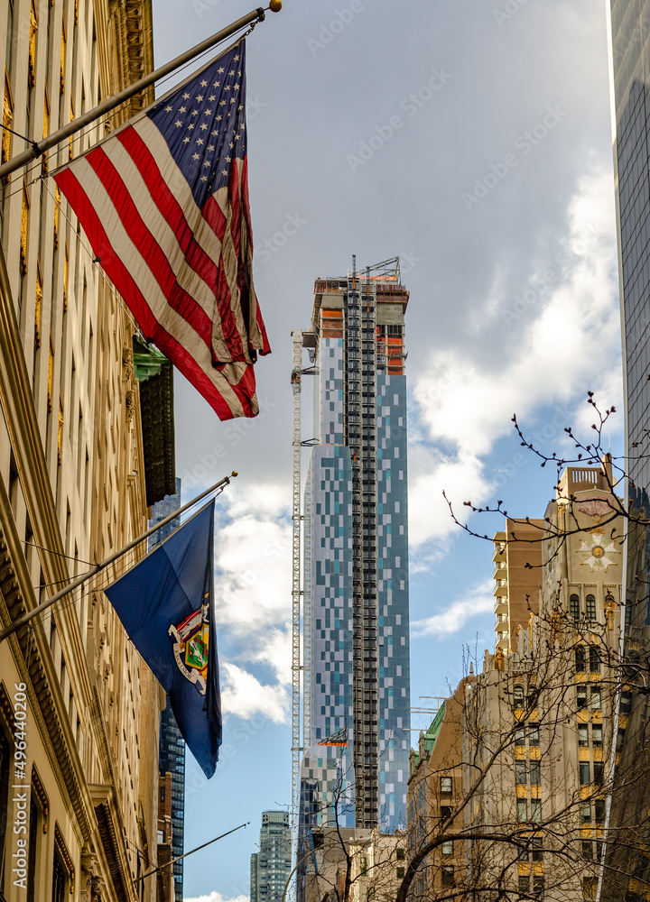 Park Hyatt Skyscraper Construction Site at W57th ST, New York City with American flag in the front, view from low angle during sunny winter day with cloudy sky, vertical