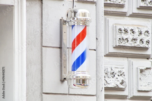the classic symbol of a barber shop - barber's pole - in the form of a spiral of white, blue and red colors on the wall of the building in which the hairdresser is located