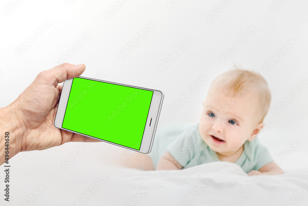 Man holding smartphone with green chromakey screen and taking photo of cute newborn baby Man holding smartphone with green chromakey screen and taking photo of cute newborn baby