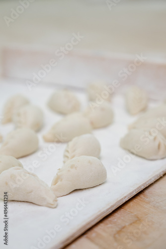 Dumplings with minced meat and dough on table sprinkled with flour.