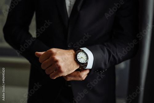 an elegant man in a suit fastens the cuffs on his shirt, looks at his watch, close up