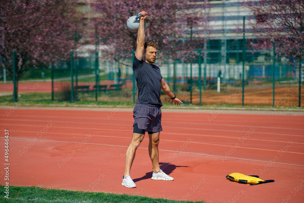 Young muscular man doing exercises with kettlebell outdoor. Weightlifting workout. Sports, fitness concept.