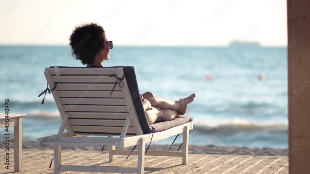 Woman in bikini lying on lounge chair on a tropical beach sun tanning. Vacation and summer travel concept Woman in bikini lying on lounge chair on a tropical beach sun tanning. Vacation and summer travel concept