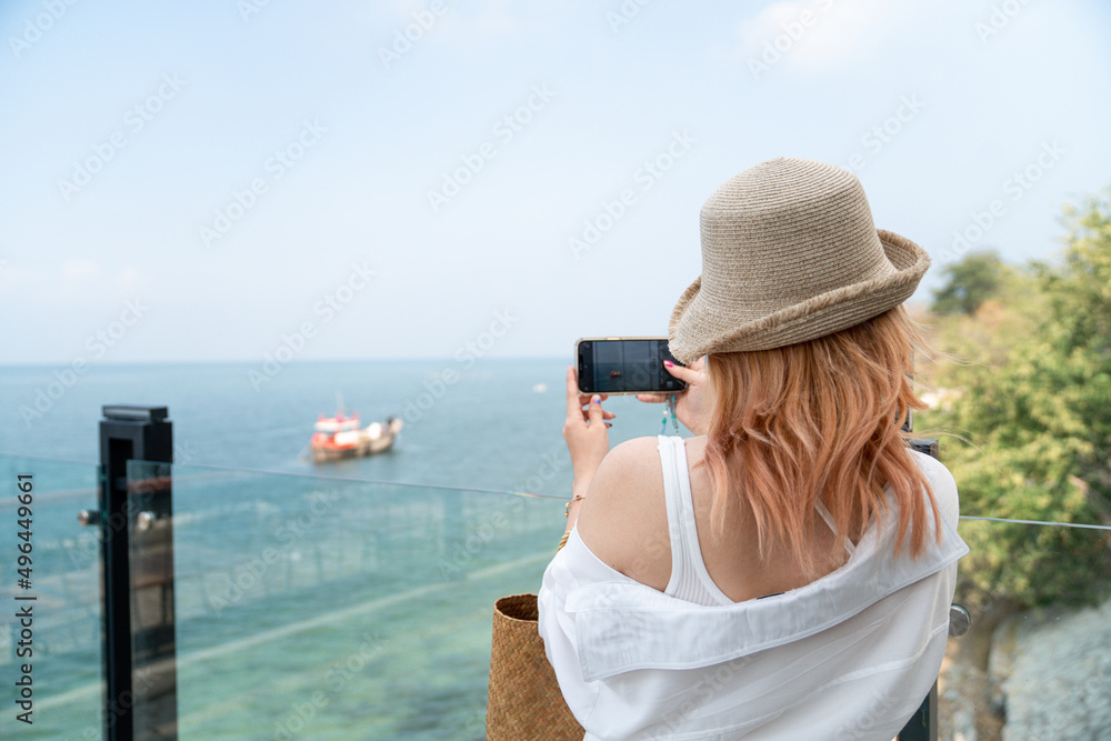 Young female taking a photo of the sea with cellphone, smartphone, travel alone