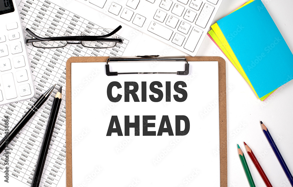 Clipboard with text CRISIS AHEAD and keyboard and chart on white background. Clipboard with text CRISIS AHEAD and keyboard and chart on white background.