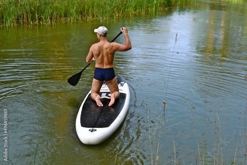 man in shorts and cap on supboard with paddle swimming in lake in summer photo