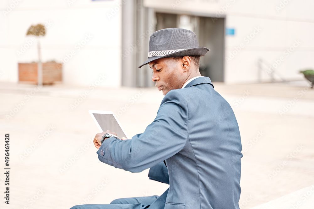gentleman using tablet pc and looks at wrist watch in the city. young business man in suit and hat working. gentleman using tablet pc and looks at wrist watch in the city. young business man in suit and hat working.