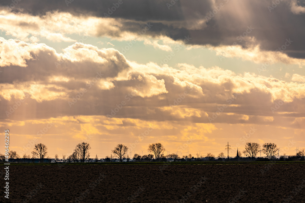 Dramatische Regenwolken und atemberaubende Sonnenstrahlen im Gegenlicht mit Windrädern und Strommasten im Hintergrund Dramatische Regenwolken und atemberaubende Sonnenstrahlen im Gegenlicht mit Windrädern und Strommasten im Hintergrund