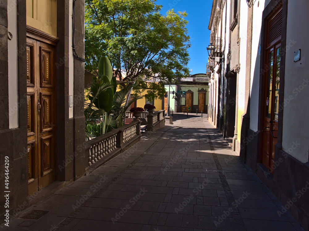 View of empty narrow alley in the historic center of Arucas on island Gran Canaria, Canary Islands, Spain on sunny day with old buildings and park.