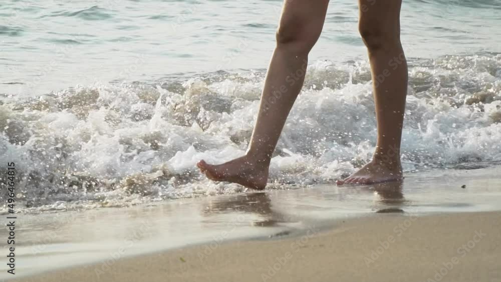 Young woman's legs close up walking and splashing on the sea shore with waves crashing and sunset reflection. Slow motion Young woman's legs close up walking and splashing on the sea shore with waves crashing and sunset reflection. Slow motion