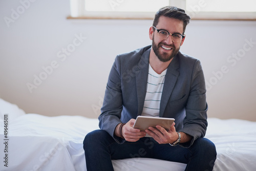 My office is wherever I am. Cropped portrait of a handsome young businessman working on a tablet while sitting on his bed at home.