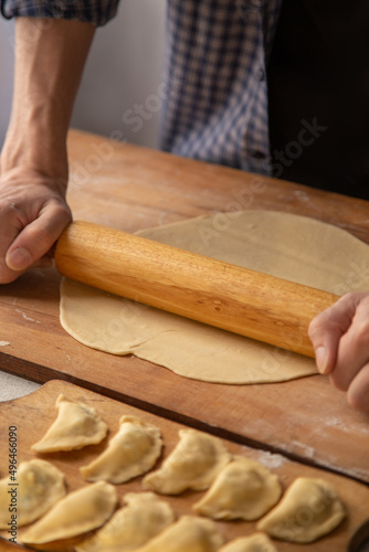 Dough rolling process. A man in a plaid shirt rolls out dough for dumplings with a rolling pin. In the foreground dumplings with cottage cheese on a cutting board
