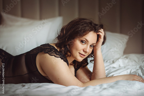 a beautiful brunette woman is lying in bed in a transparent lace bodysuit
