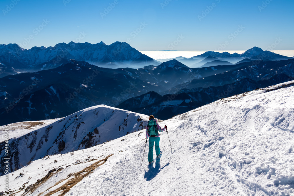 Active woman snow shoe hiking on a trail with scenic view on snow capped mountain peaks of Karawanks in Carinthia, Austria. Ski tour. Julian Alps. Sunny winter day. Freedom. Winter wonderland,Hochobir
