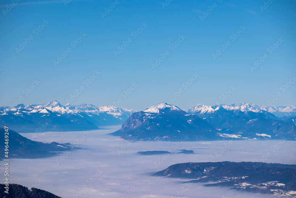 Panoramic view from Hochobir on snow capped mountain peaks of Karawanks in Carinthia, Austria. Julian Alps. Winter wonderland in the Austrian Alps, Europe. Valley covered with clouds. High Tauern Alps