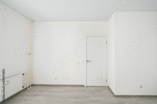 Empty room with laminate flooring and newly painted white wall in background.