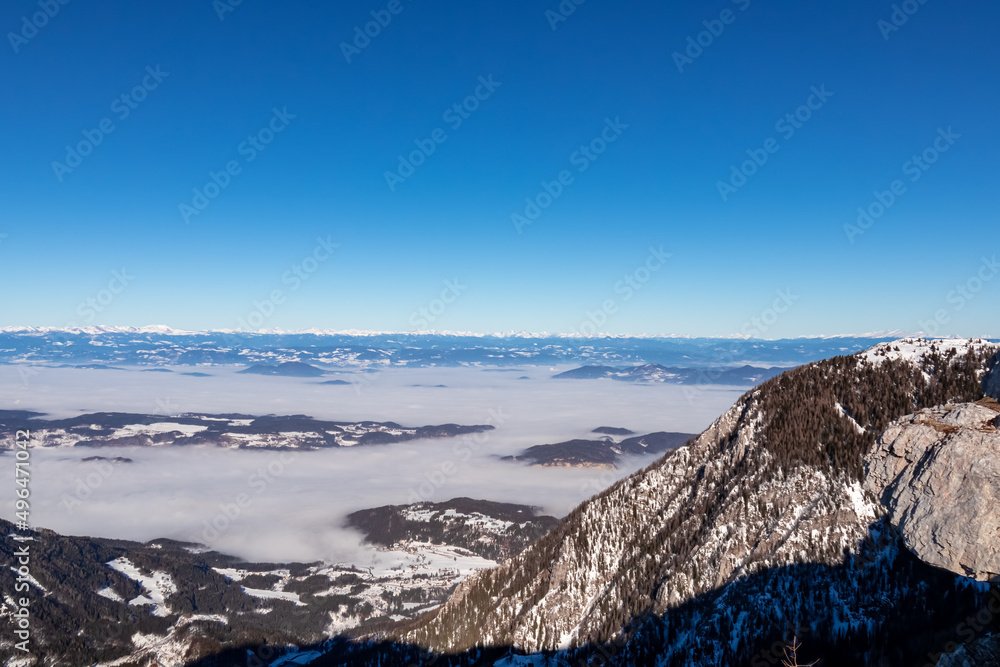 Panoramic view from Hochobir on snow capped mountain peaks of Karawanks in Carinthia, Austria. Julian Alps. Winter wonderland in the Austrian Alps, Europe. Valley covered with clouds. High Tauern Alps