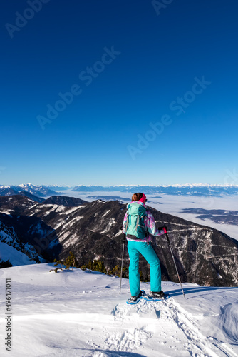 Active woman snow shoe hiking on a trail with scenic view from Hochobir on mountain peaks of Karawanks in Carinthia, Austria. Ski tour. Sunny winter wonderland day. Freedom. Valley covered with clouds