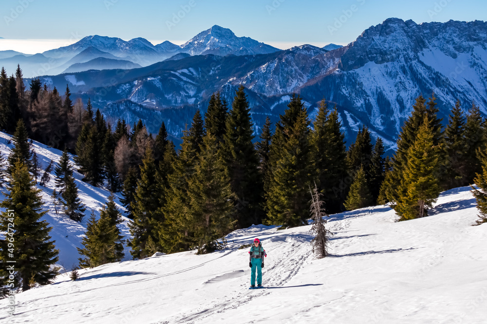 Active woman snow shoe hiking on a trail with scenic view on snow capped mountain peaks of Karawanks in Carinthia, Austria. Ski tour. Julian Alps. Sunny winter day. Freedom. Winter wonderland,Hochobir