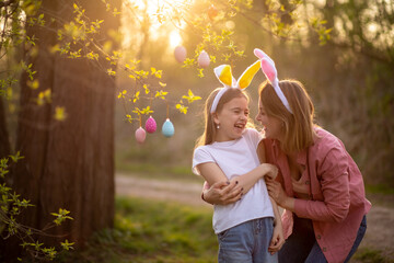 beautiful and happy mom and daughter in bunny ears decorate the tree with easter eggs. happy family celebrating easter