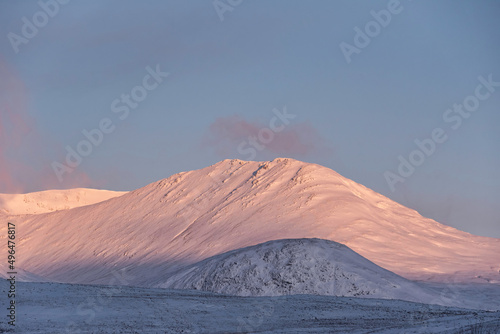Majestic Alpen Glow hitting mountain peaks in Scottish Highlands during stunning Winter landscape sunrise