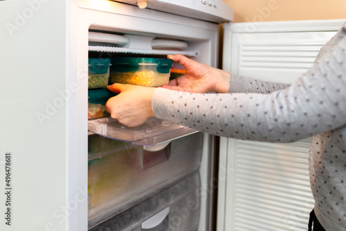 Woman taking containers with frozen corn out from freezer.