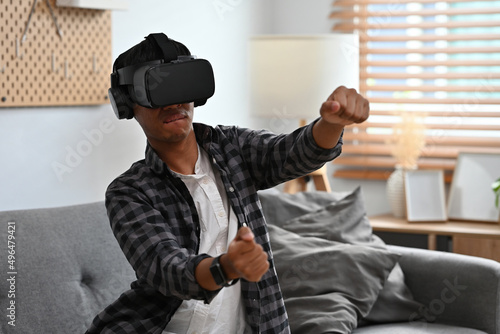 A portrait of a man sitting on a couch in a living room  wearing a virtual reality technology goggle and acting driving  for future  game and technology concept.