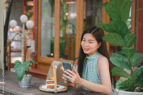 Smiling beautiful Asian woman eating green tea and snacks in a cafe to relax on a leisurely day. Look at the cell phone to check the work. She is an Asian business woman.