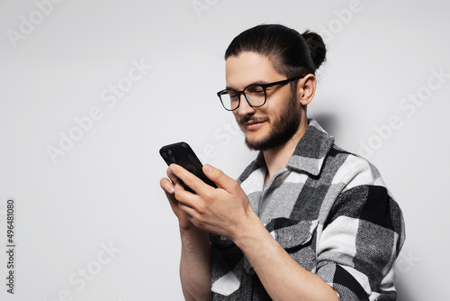 Studio portrait of young smiling man with hair bun, texting on smartphone.