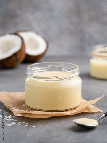 Coconut condenced milk with coconut shred and white chocolate in glass jar. Sweet vegetarian dessert. Grey concrete background. Homemade delicious spread or paste for breakfast. Close up food photo