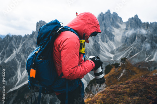 Photographer with red softshell jacket, backpack and radio station checking photos while hiking in the mountains in cold weather. Hiker using digital camera while trekking mountain trail photo