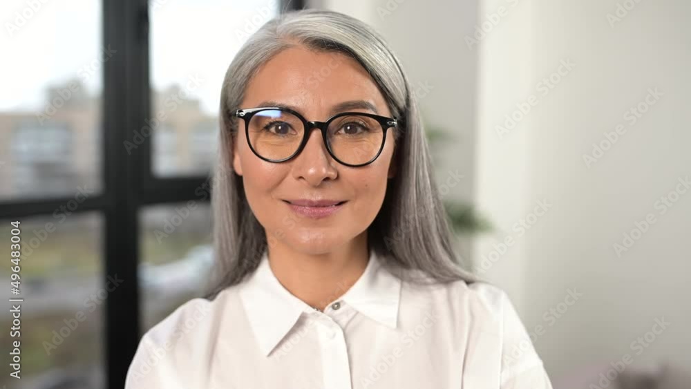 Serious and strict old senior business woman wearing smart casual shirt and stylish eyeglasses standing with arms crossed in modern office space. Mature bossy lady, elderly purposeful leader concept Serious and strict old senior business woman wearing smart casual shirt and stylish eyeglasses standing with arms crossed in modern office space. Mature bossy lady, elderly purposeful leader concept