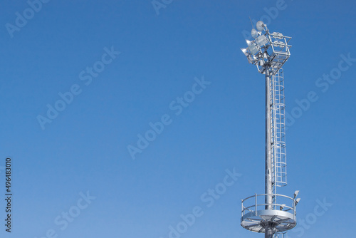 High metal mast with spotlights against a clear sky.