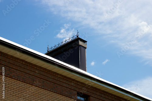 A roof with a chimney on the background of a blue summer sky. © Sofya