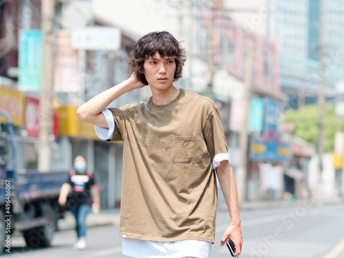 Photography Portrait of handsome Chinese young man with black curly hair in brown T-shirt and pants walking on Shanghai old town street with hand on his head looks lost, front view of modern young people