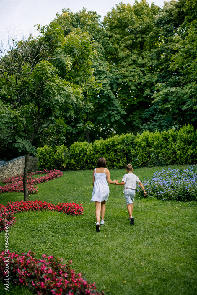 Smiling mother and son are walking in the park together in summer in light clothes. Soft sunset light. Smiling mother and son are walking in the park together in summer in light clothes. Soft sunset light.