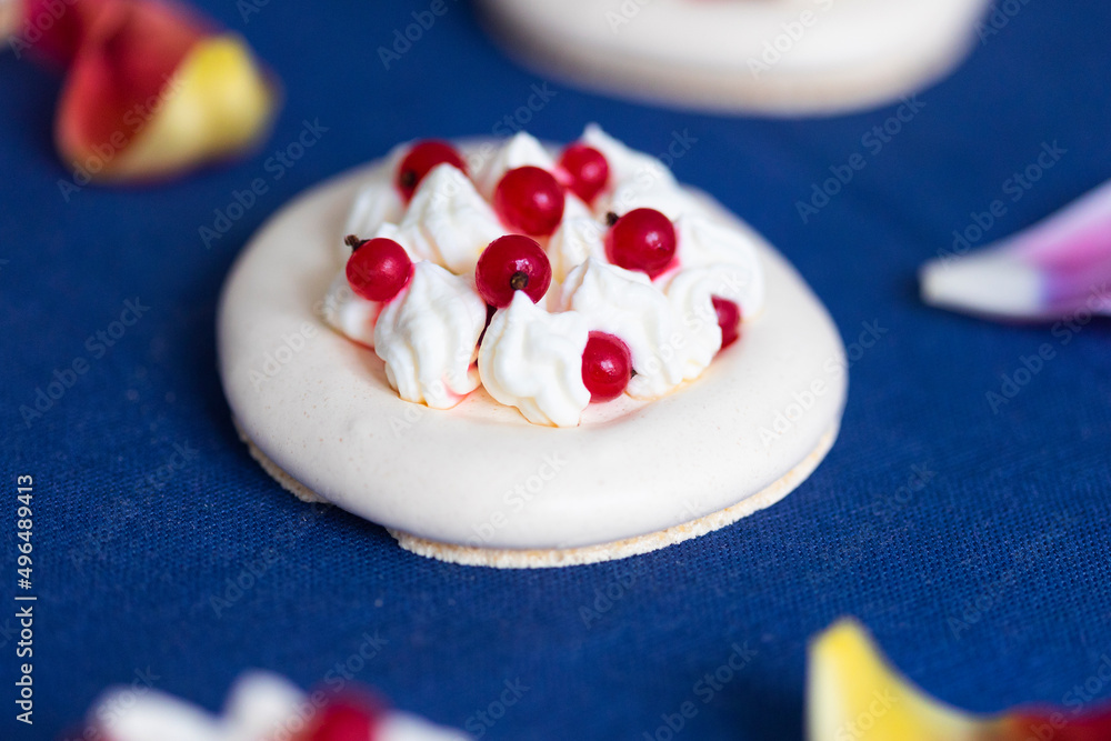 Meringue cakes called Pavlova cake with Pavlova cake and red currant berries on deep blue tablecloth with pink petals Meringue cakes called Pavlova cake with Pavlova cake and red currant berries on deep blue tablecloth with pink petals